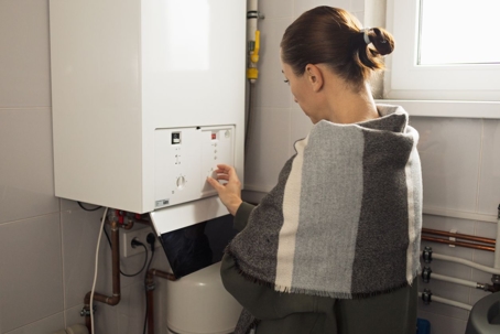 A woman adjusts the settings of a wall-mounted boiler